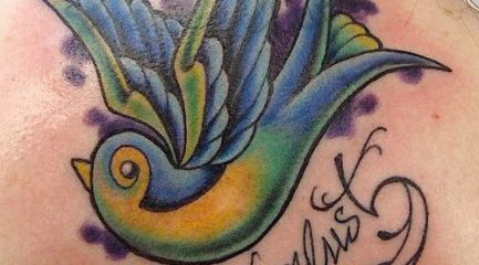 Wanderlust colorful swallow tattoo on back of girl’s neck