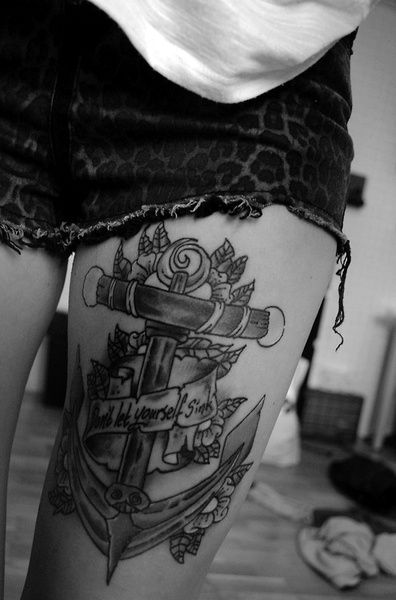 Big anchor tattoo on girl’s thigh with flowers and banner