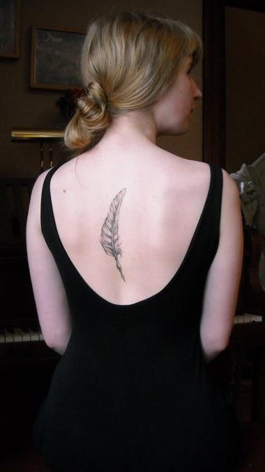 Black feather tattoo in middle of girls back