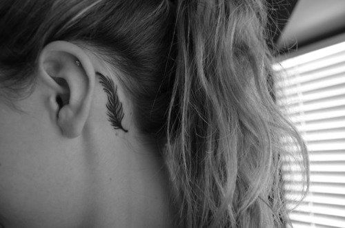 Small black feather tattoo behind girls ear
