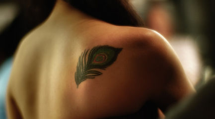 Small peacock feather on back of girls shoulder